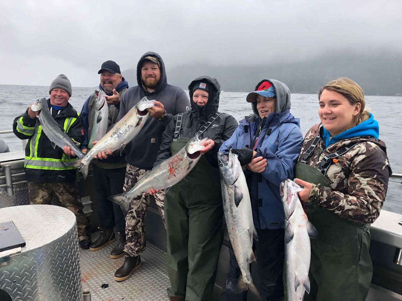 Six guests on the deck of the charter boat holding up a limit of salmon in Southeast Alaska