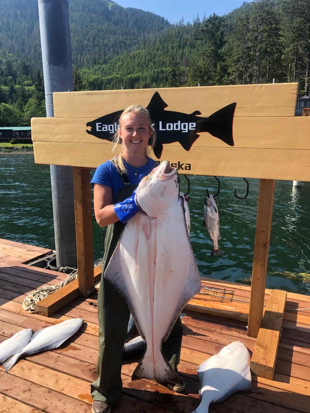Guest holding a halibut beside the carved Eagle Rock Lodge sign on the dock in Craig, Alaska