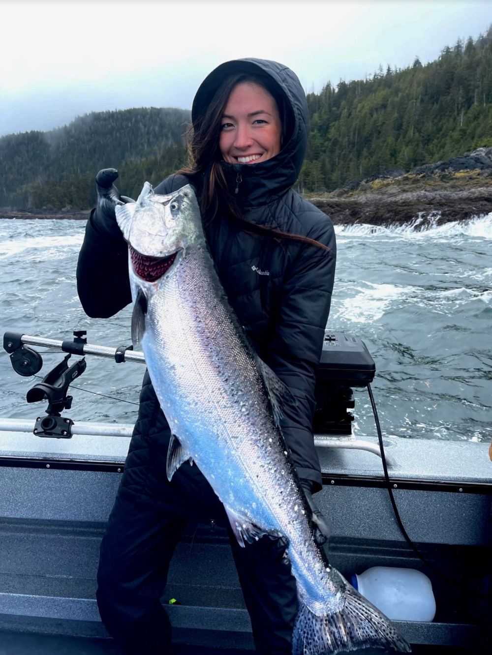 Angler in rain gear holding a bright silver salmon aboard the charter boat off Craig, Alaska
